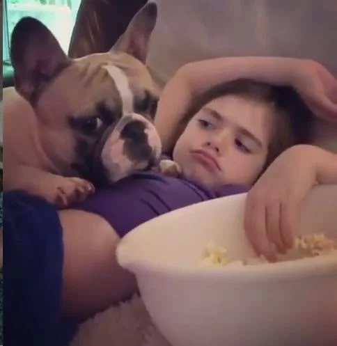 A girl eating popcorn with Frenchie Pug